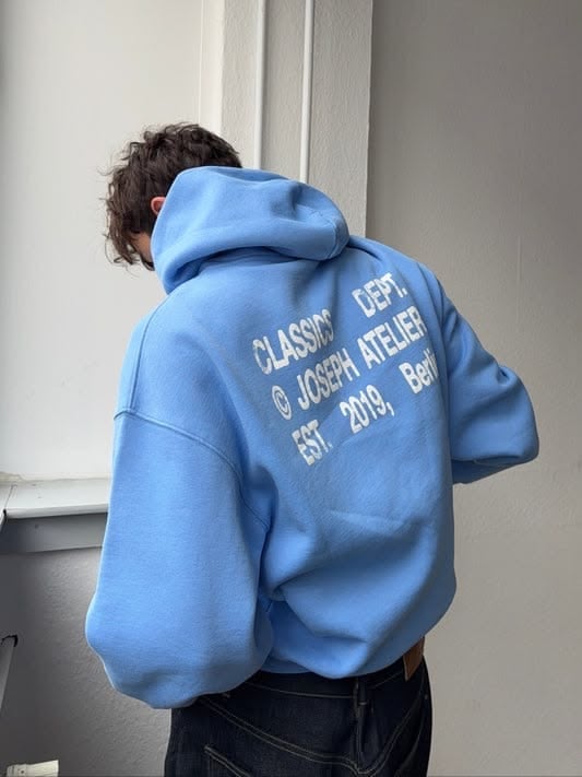 Person wearing a blue hoodie with Glasgow and Joseph Atelier text printed on the back